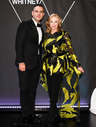 Two guests at a Whitney event wearing a black tuxedo and a flowing black and yellow ensemble.