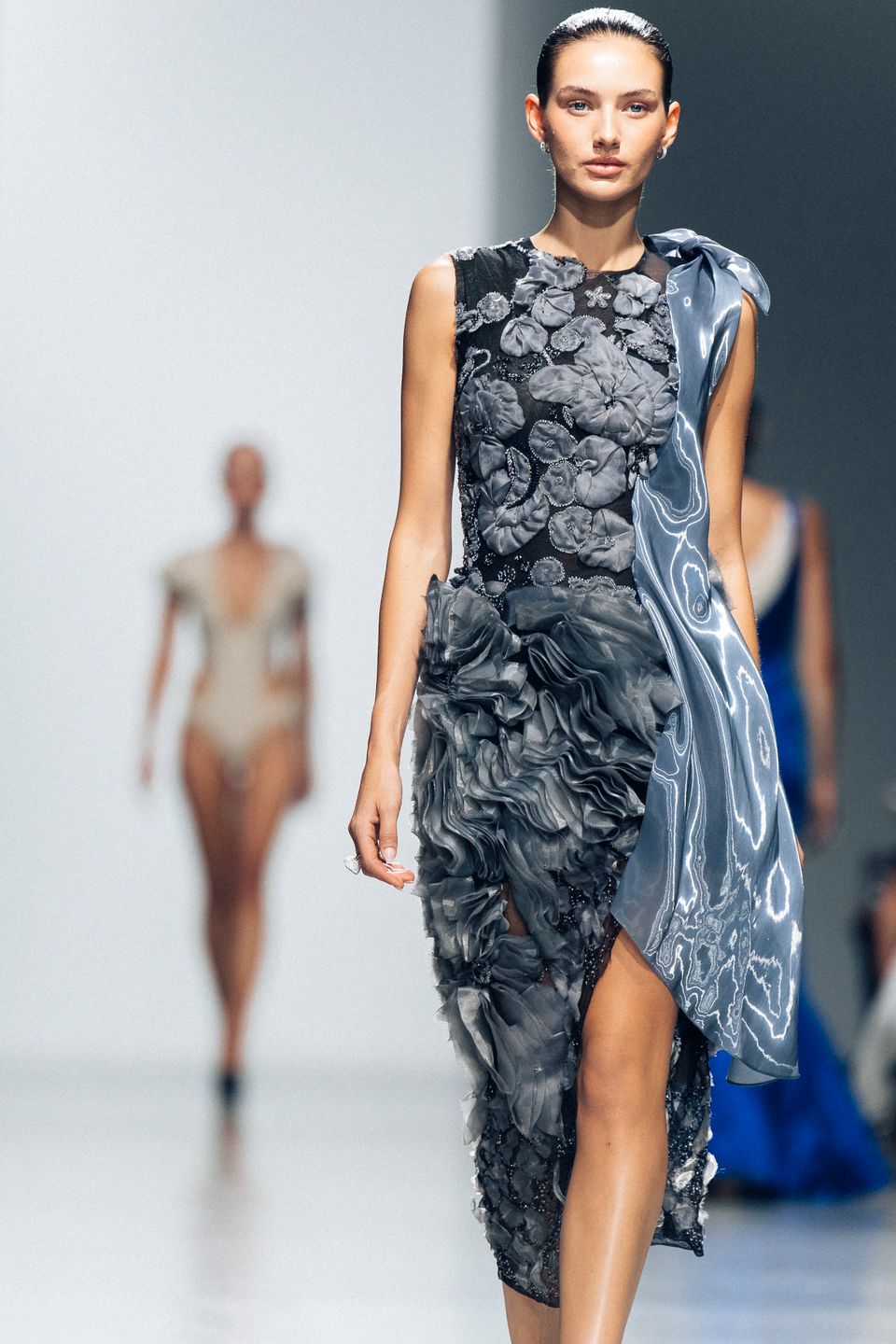 Model in a sculptural blue dress on the runway
